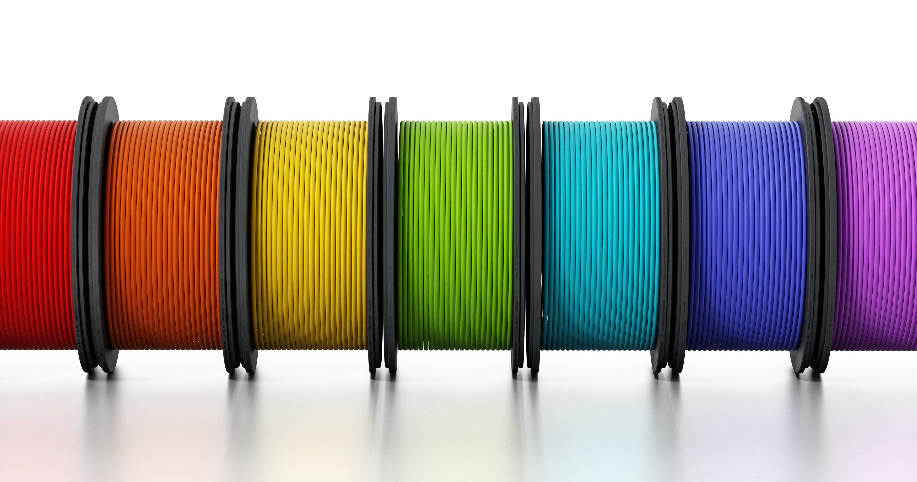 Six spools of filament in orange, yellow, green, light blue, blue, and purple, arranged side by side on a white surface.