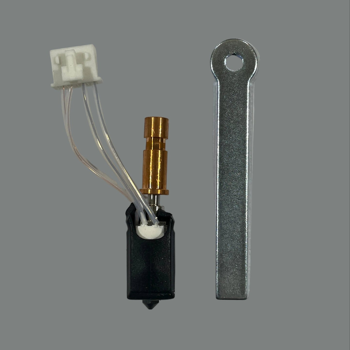 A small replacement appliance part set on a light gray background, featuring a black plastic component with a white multi-pin connector and a brass-colored tube, alongside a flat silver metal piece with a loop at one end.