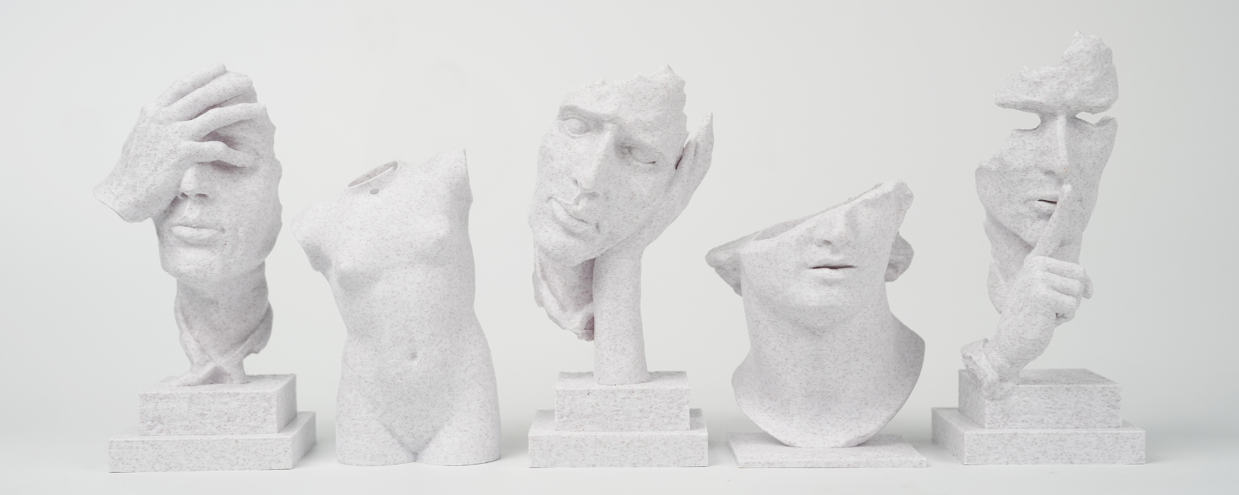 Five fragmented white marble sculptures of human faces and torsos are displayed on rectangular pedestals against a plain white background.