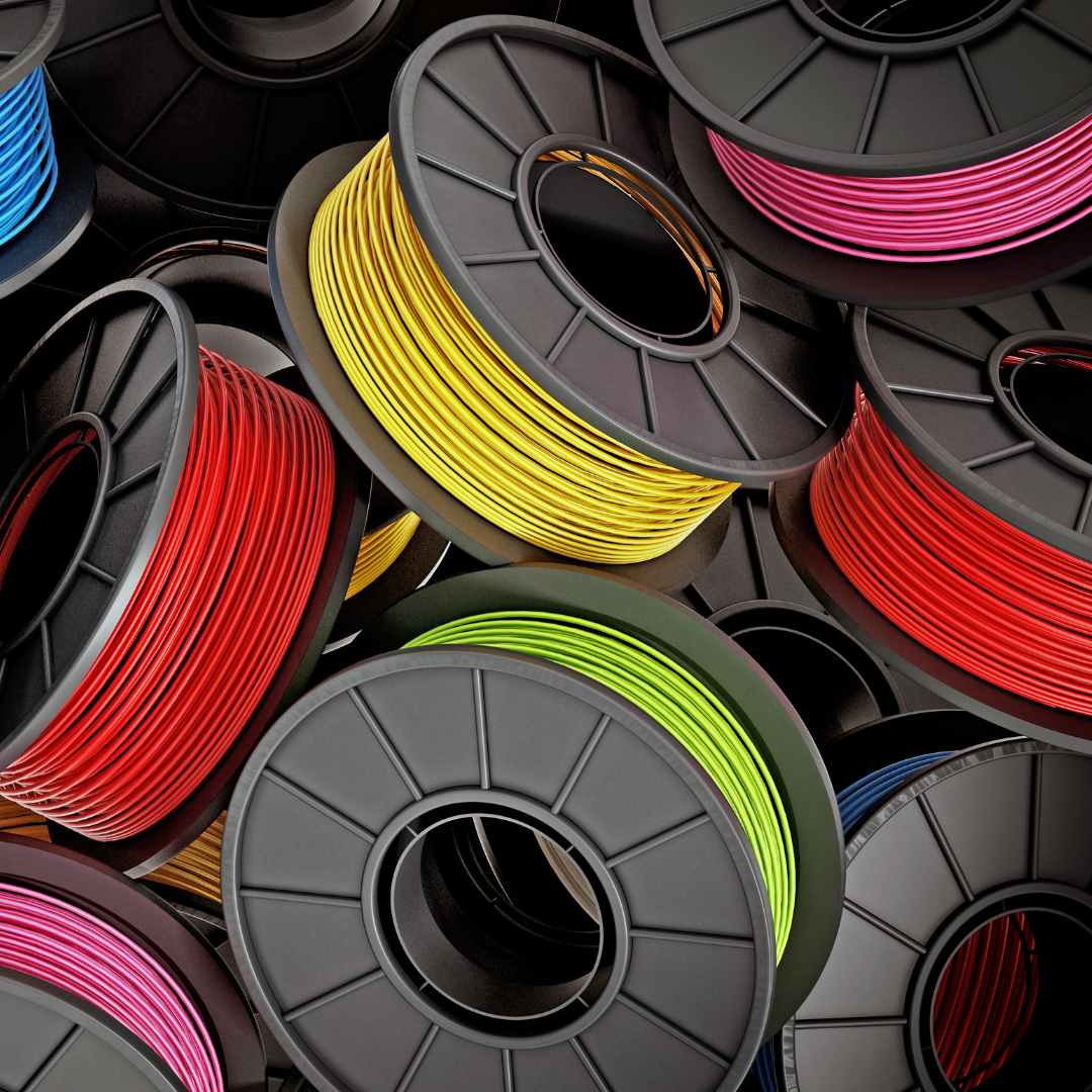 Multiple spools of 3D printer filament in various colors, including blue, red, yellow, white, and pink, are stacked and overlapping.
