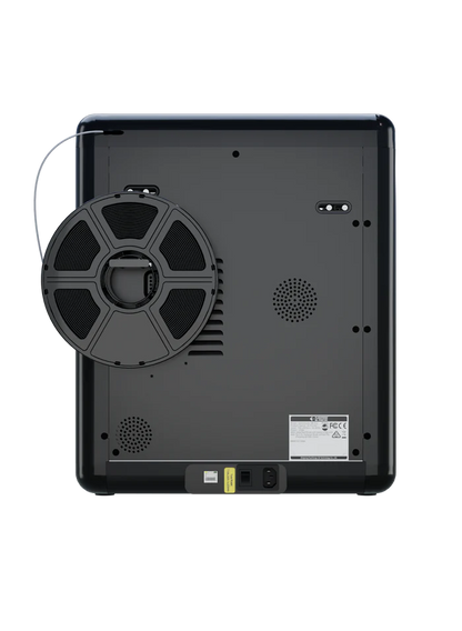 The image displays the back of the FlashForge Adventurer 5M Pro by FlashForge, featuring a circular spool, ventilation grills, and a power socket—engineered for quick setup and safe use in both home and school settings.