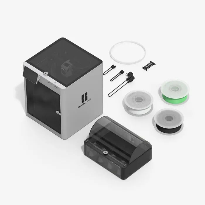 The Bambu Lab X1C 3D Printer from Bambu Lab is displayed with filament spools, a filament dryer, power supply, cables, and accessories—everything needed for high quality prints arranged neatly on a white surface.