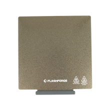 The PEI Coating Platform for the Adventurer 5M Series by Flashforge is a textured square build plate that enhances adhesion, complete with safety icons and branding at the bottom.