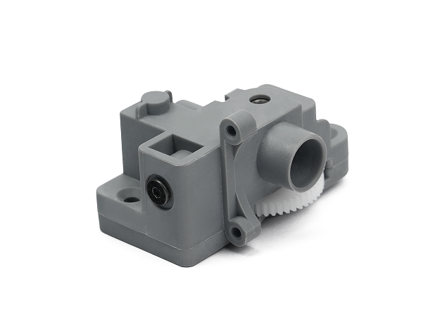 Gray mechanical device featuring a cylindrical protrusion and two visible holes, with a white gear partially visible on one side—an essential element of the Flashforge Filament Feeding Assembly for the Adventurer 5M Series, designed for 3D printing purposes.