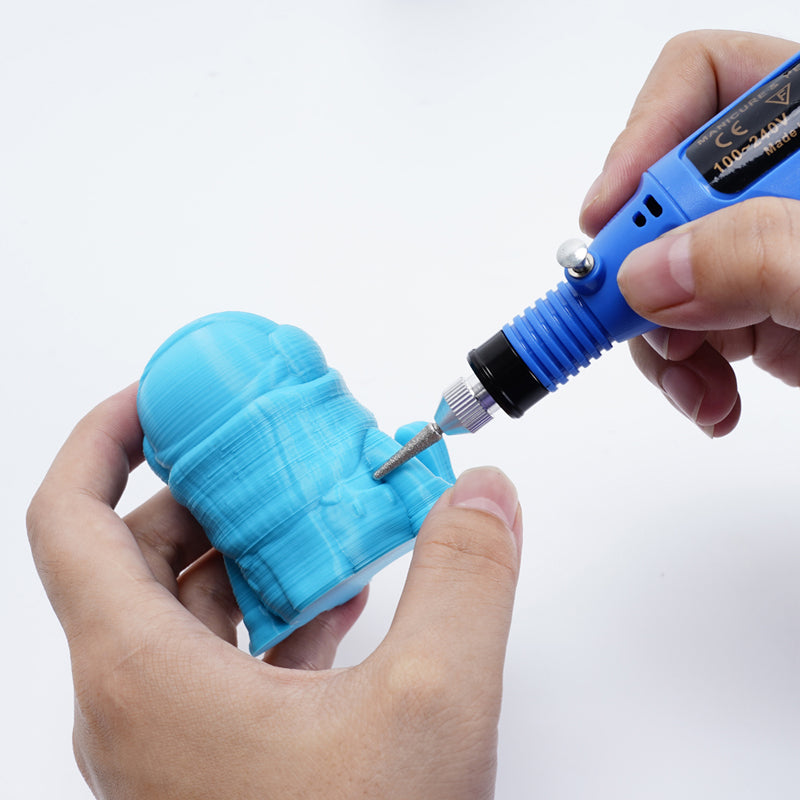 A DIY enthusiast expertly uses a blue Electric Sander Mini Electric Grinder Tool USB Adjustable Speed with Heads from 3D Printing Perth - Cirrus Link to engrave intricate details into a small blue 3D-printed figurine.