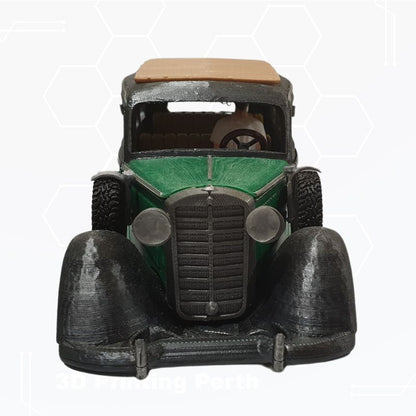 A 3D-printed model of a classic car, specifically an STL File: 1930 Mercedes Vehicle by Gordon Nezich, featuring a green body with black fenders and a brown roof, viewed from the front.