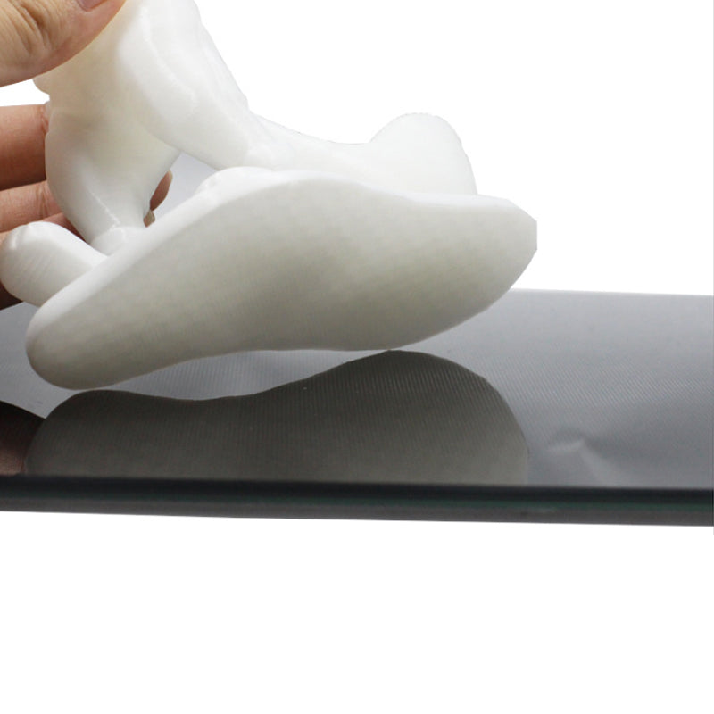 A hand holds a white figurine created with the help of the Lattice Platform Glass Platform, 4mm thick, from 3D Printing Perth - Cirrus Link, resting on a flat, dark surface.