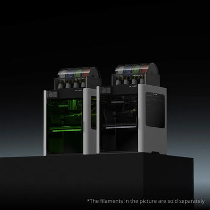 Two Bambu Lab H2D 3D printers with transparent filament compartments sit side by side on a black platform, perfect for multi-material printing; note: filaments are sold separately.