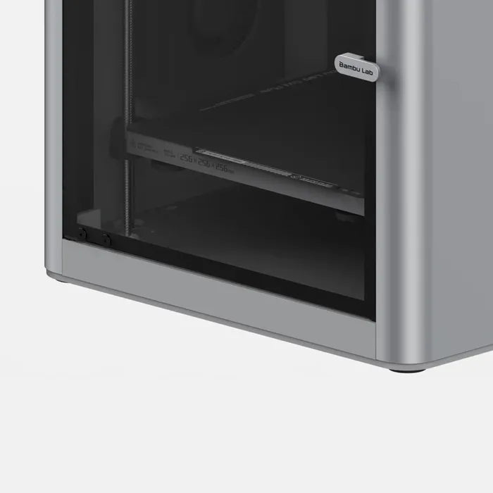 Close-up of the lower front corner of the Bambu Lab X1C 3D Printer by Bambu Lab, featuring its transparent door and a view of the build chamber and CoreXY system for high-quality printing.