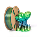 A spool of Toyar PLA Silk Rainbow 1.75mm filament sits beside a 3D-printed abstract tree, both displaying the vibrant, shimmering colors of this Toyar product—ideal for creative and colorful 3D printing projects.