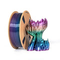 A spool of Toyar PLA Silk Rainbow 1.75mm filament stands next to a shiny, multicolored 3D-printed sculpture with a wavy, organic shape on a white background.