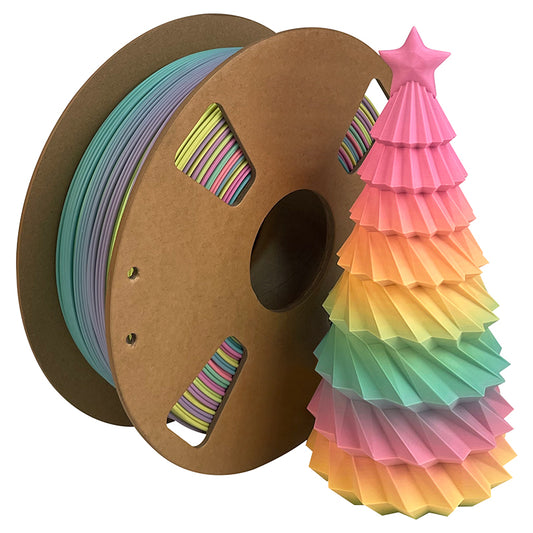 A spool of Toyar PLA Matte Rainbow 1.75mm Filament sits next to a small, pastel, star-topped folded paper tree, ready for matte finish 3D printing.