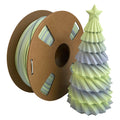 A spool of Toyar PLA Matte Rainbow 1.75mm Filament with a smooth matte finish sits next to a small, folded gradient Christmas tree topped with a star.