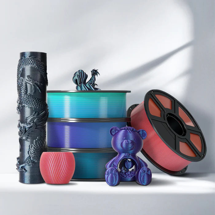 Four Flashforge PLA 1.75mm 3D Printing Filament spools in multiple colours are displayed with 3D printed models—a dragon column, rooster, vase, and teddy bear—demonstrating smooth surface finish and reliable extrusion on a white surface.