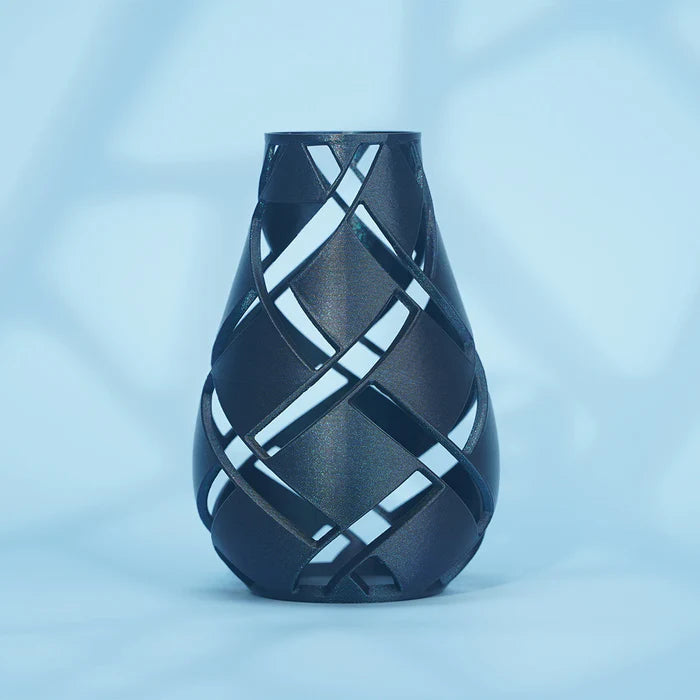 A black vase, 3D printed with Flashforge PLA 1.75mm Filament, features an open lattice design and smooth finish. It stands upright against a light blue background with soft shadows. Brand: Flashforge.