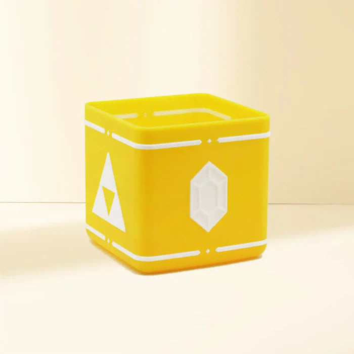 A yellow, square container 3D printed with Flashforge PLA Pro 1.75mm filament features white rupee symbols and triangle designs on its sides, set on a light surface with a neutral background.