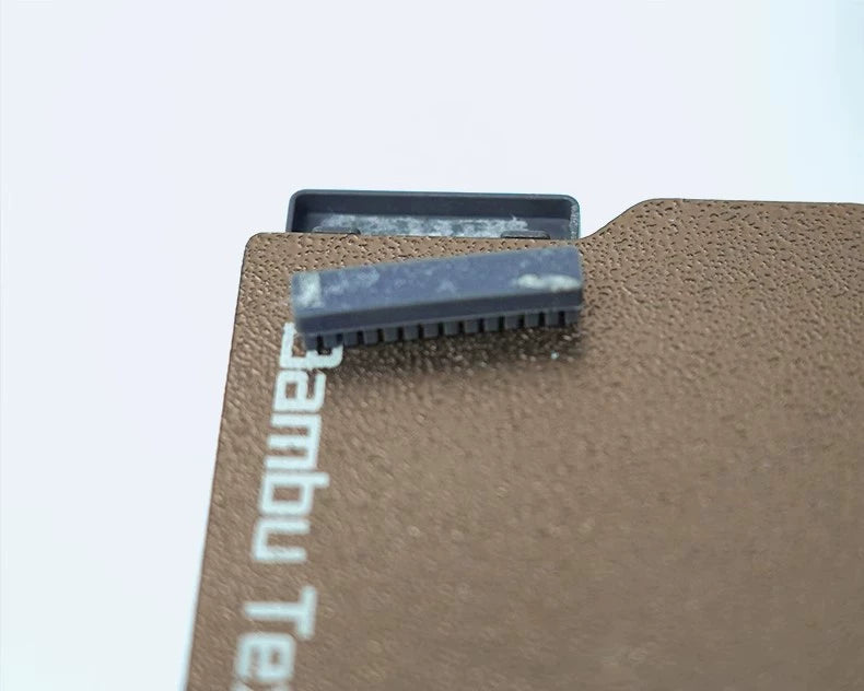 A close-up of a textured surface reveals the edge of a small, rectangular component from the Silicone Nozzle Wiper Brush Set (3-Pack) by Bambu Lab, crucial for maintaining the A1 Mini 3D Printer.