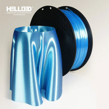 A spool of Hello3D PLA SILK Colour 1.75mm filament sits beside a metallic blue, cloth-like 3D print, showcasing the luxury finishes possible with premium PLA SILK from Hello3D.