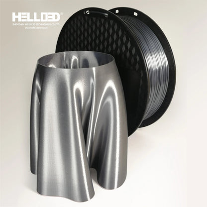 A spool of Hello3D PLA SILK Colour 1.75mm filament in dark gray stands behind a metallic, wavy 3D-printed object—perfect for luxury quality prints.