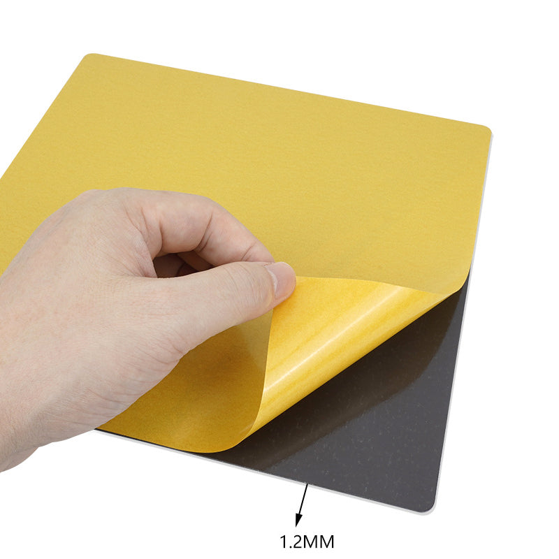 A hand elegantly peels a yellow adhesive sheet from a square black surface on the 3D Printing Perth - Cirrus Link Bambu Lab X1 Magnetic Steel 268*258mm Print Surface, revealing the sleek steel film beneath.